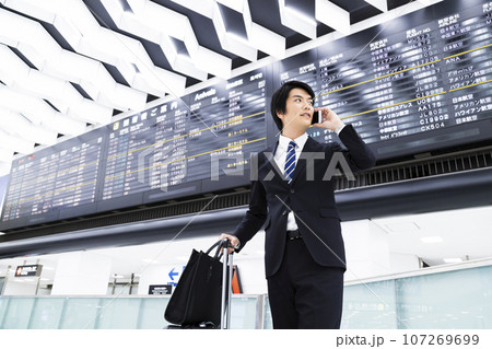 スマホを見ながら空港から出張をする若いビジネスマン 107269699