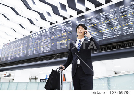 スマホを見ながら空港から出張をする若いビジネスマン 107269700