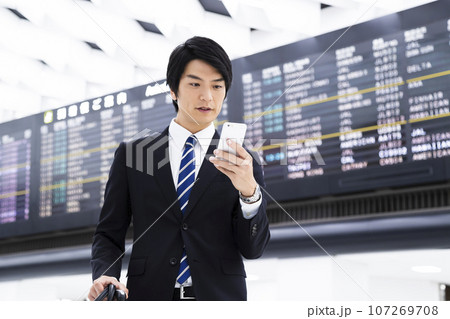 スマホを見ながら空港から出張をする若いビジネスマン スマホを見ながら空港から出張をする若いビジネスマン 107269708