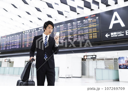 スマホを見ながら空港から出張をする若いビジネスマン スマホを見ながら空港から出張をする若いビジネスマン 107269709