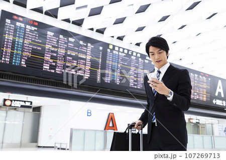 スマホを見ながら空港から出張をする若いビジネスマン 107269713