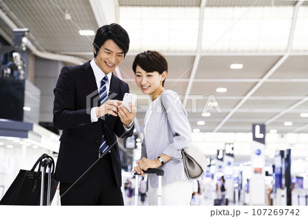 スマホを見ながら空港から出張をする若い男女のビジネスマン スマホを見ながら空港から出張をする若い男女のビジネスマン 107269742