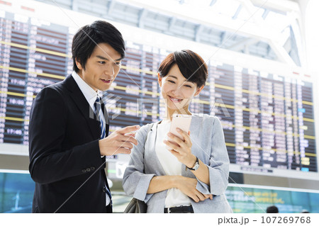 スマホを見ながら空港から出張をする若い男女のビジネスマン スマホを見ながら空港から出張をする若い男女のビジネスマン 107269768