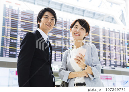 スマホを見ながら空港から出張をする若い男女のビジネスマン 107269773