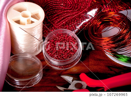 Tools for making handmade jewelry. Box with red beads on an old wooden background. Handmade accessories. View from above 107269965