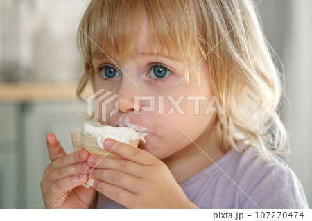 Baby girl enjoying ice cream. Pretty little toddler eating an ice-cream indoors, at home. Dining room background. Small child eats plombir and cream messy on her mouth. Cute kid with tasty sweet food. Baby girl enjoying ice cream. Pretty little toddler eating an ice-cream indoors, at home. Dining room background. Small child eats plombir and cream messy on her mouth. Cute kid with tasty sweet food. 107270474