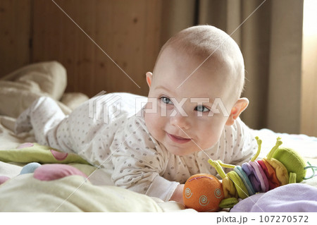 Smiling baby girl learning to crawl and playing with colorful toys in white sunny bedroom. 107270572