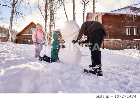 A family builds a snowman out of white snow in the yard in winter. 107271474