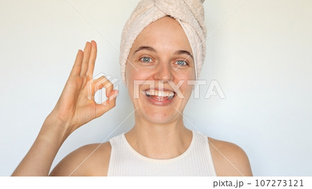 Happy joyful beautiful young woman with bath towel on head isolated over white background showing ok gesture approved sign likes her morning routine looking smiling at camera. 107273121