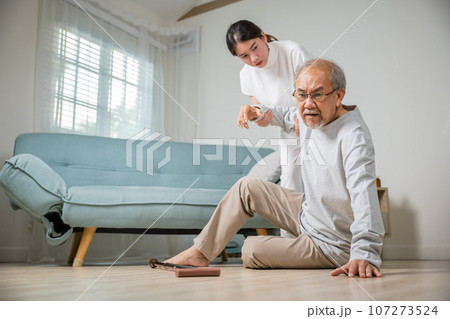 Dizziness elderly old man falling down lying on floor with walking stick and assistant nurse help to support, senior father fall on the ground and his daughter helping wake up and get up, accident 107273524