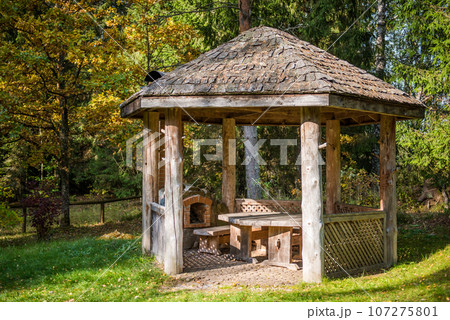 Wooden gazebo and brick stove for cooking food outdoors. Public park with picnic table and bench 107275801