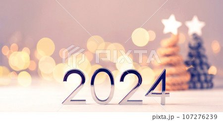 Metal numbers 2024 on a white table with Christmas trees and bokeh lights. Happy New Year 2024 is coming concept. 107276239