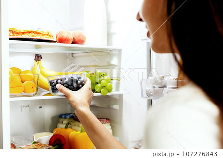 Woman hand taking or picks up box of blueberry out of open refrigerator, fridge Woman hand taking or picks up box of blueberry out of open refrigerator, fridge 107276843