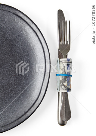 Gray ceramic plate and fork with knife wrapped in hundred dollar bills isolated on white background. Expensive restaurant 107278566