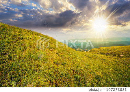green grass on hillside meadow in high mountains under the cloudy blue sky at sunset. beautiful countryside scenery in evening light 107278881
