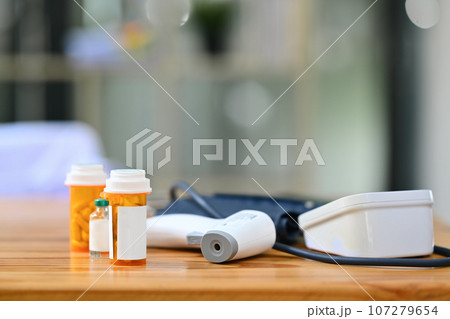 Pills bottles, blood pressure monitor and infrared thermometer on wooden table. Medicine and healthcare concept Pills bottles, blood pressure monitor and infrared thermometer on wooden table. Medicine and healthcare concept 107279654