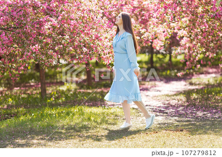 Happy girl in blue dress, is standing in a pink blooming garden Happy girl in blue dress, is standing in a pink blooming garden 107279812
