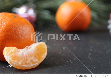 mandarin whole in the peel and a slice of fruit lie side by side on a black background next to a branch of spruce and a silver cone. New Year and Christmas. holiday attribute mandarin whole in the peel and a slice of fruit lie side by side on a black background next to a branch of spruce and a silver cone. New Year and Christmas. holiday attribute 107280257
