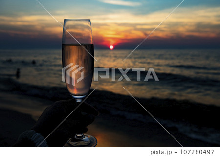 close up of two white wine glasses cheering with beach sunset background 107280497