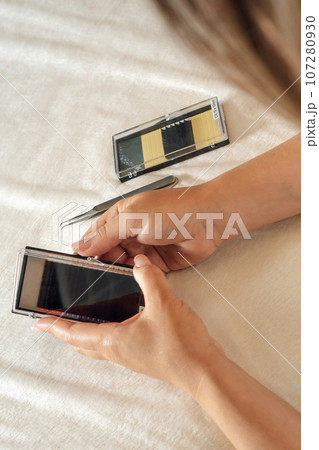 Woman opening palette of fake eyelashes and preparing for lash extension procedure. Tools lying on couch near master. 107280930