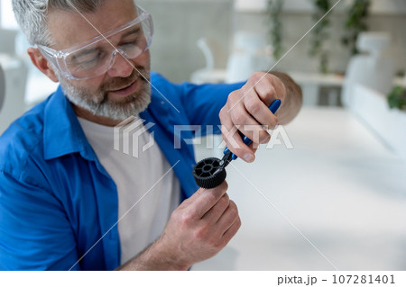 Mature man holding fixing machine part modeling with 3D printer. Mature man holding fixing machine part modeling with 3D printer. 107281401