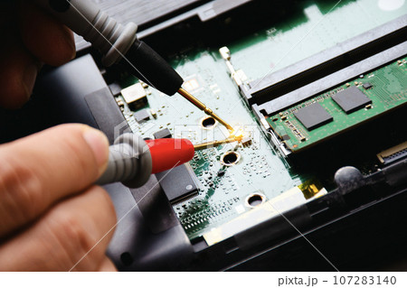 Electrician checks electronic circuit board by probe of digital multimeter. Appliance repair concept 107283140
