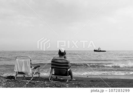 Man sitting on chair is watching an old ship sailing on sea Man sitting on chair is watching an old ship sailing on sea 107283299