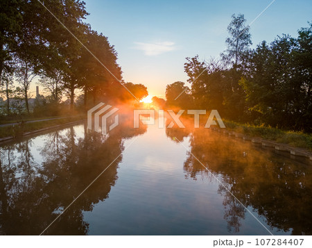 Mystical Morning: Fiery Fog Over Canal at Sunrise Mystical Morning: Fiery Fog Over Canal at Sunrise 107284407