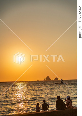 （静岡県）西伊豆・大田子海岸の夕陽を眺めるカップル 107285621