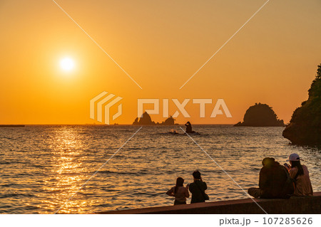 （静岡県）西伊豆・大田子海岸の夕陽を眺めるカップル 107285626