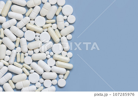 Mix of white medical capsules and pills on light blue top view, copy space. Medicinal treatment Mix of white medical capsules and pills on light blue top view, copy space. Medicinal treatment 107285976