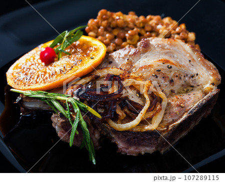 Baked pork shank with lentils and grilled orange 107289115