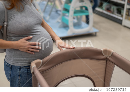 Caucasian pregnant woman chooses a playpen crib in a children's store.  107289735