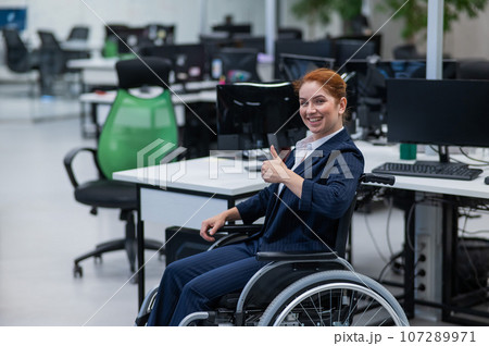 Caucasian woman in wheelchair showing thumb up while sitting in open space office. Caucasian woman in wheelchair showing thumb up while sitting in open space office. 107289971