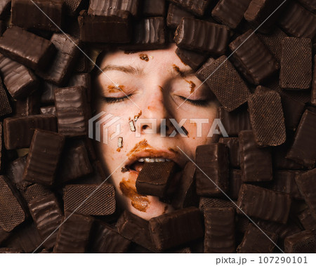 The face of a caucasian woman surrounded by sweets. The girl is smeared in sweets.  107290101