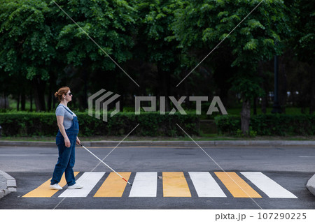 Blind pregnant woman crosses the road at a crosswalk with a cane. Blind pregnant woman crosses the road at a crosswalk with a cane. 107290225