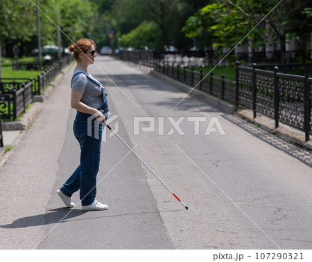 Blind pregnant woman crosses the street with the help of a tactile cane. Blind pregnant woman crosses the street with the help of a tactile cane. 107290321