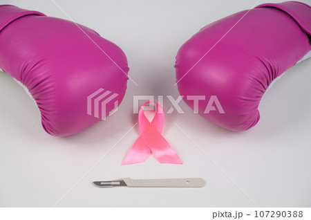 Pink boxing gloves, a surgical scalpel and a pink ribbon on a white background. The concept of fighting breast cancer.  107290388