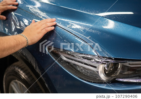 The master in the car service applies a protective armor film to the car body.  107290406