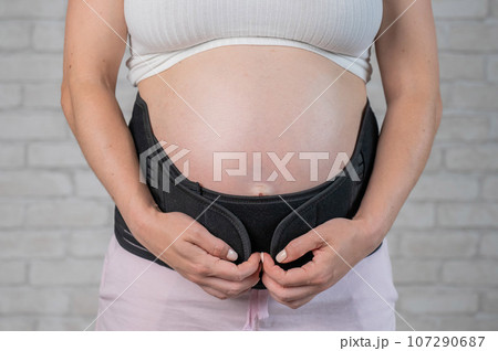 A pregnant woman puts on a black two-piece bandage. Cropped tummy. A pregnant woman puts on a black two-piece bandage. Cropped tummy. 107290687