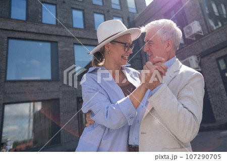 An elderly couple in love dances outdoors. A gray-haired man and a mature woman laugh and hug. An elderly couple in love dances outdoors. A gray-haired man and a mature woman laugh and hug. 107290705