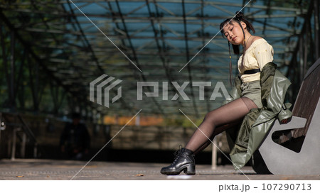A young Asian woman sits on a bench at the subway exit.  107290713
