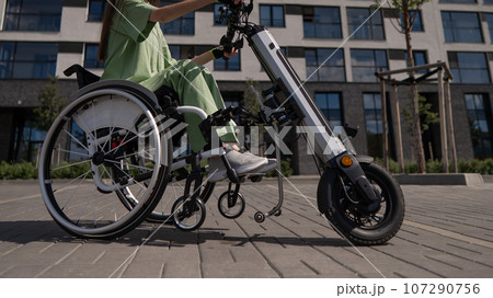 A woman in a wheelchair with an assistive device for manual control. Electric handbike. A woman in a wheelchair with an assistive device for manual control. Electric handbike. 107290756