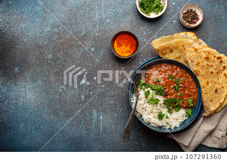 Traditional Indian Punjabi dish Dal makhani with lentils and beans in black bowl served with basmati rice, naan flat bread, fresh cilantro and spoon on blue concrete rustic table top view. Copy space 107291360