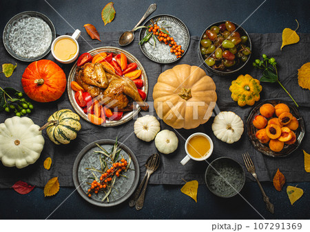 Thanksgiving festive table composition with roasted turkey, pumpkins, vegetable salad, fruit, orange beverage. Thanksgiving celebration dinner with traditional autumn meals on rustic dark table Thanksgiving festive table composition with roasted turkey, pumpkins, vegetable salad, fruit, orange beverage. Thanksgiving celebration dinner with traditional autumn meals on rustic dark table 107291369