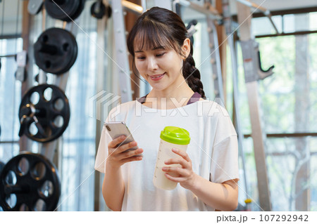 プロテインを持ちながらスマートフォンを使う女性 プロテインを持ちながらスマートフォンを使う女性 107292942