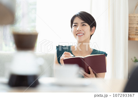リビングで手帳を見る女性 107293367