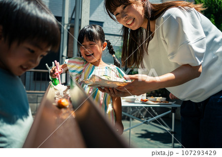 お庭で雨どい流しそうめんをする家族 107293429