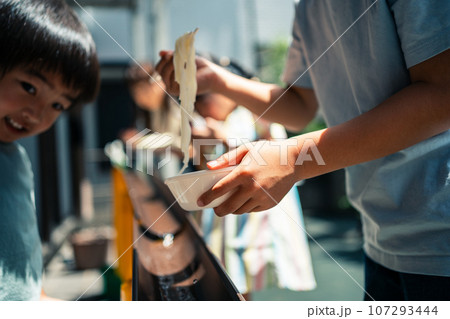 お庭で雨どい流しそうめんをする家族 107293444