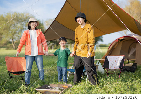 キャンプ場で手を繋いで遊ぶ笑顔のファミリー 107298226